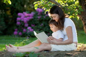 Mother and boy, reading a book, summertime in a garden, nice sunset light